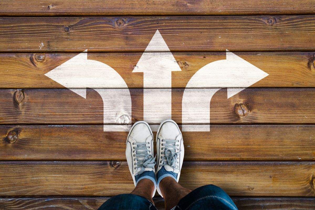 A pair of feet with sneakers on, with three arrow, one points forward and the others left and right. All on a wooden floor